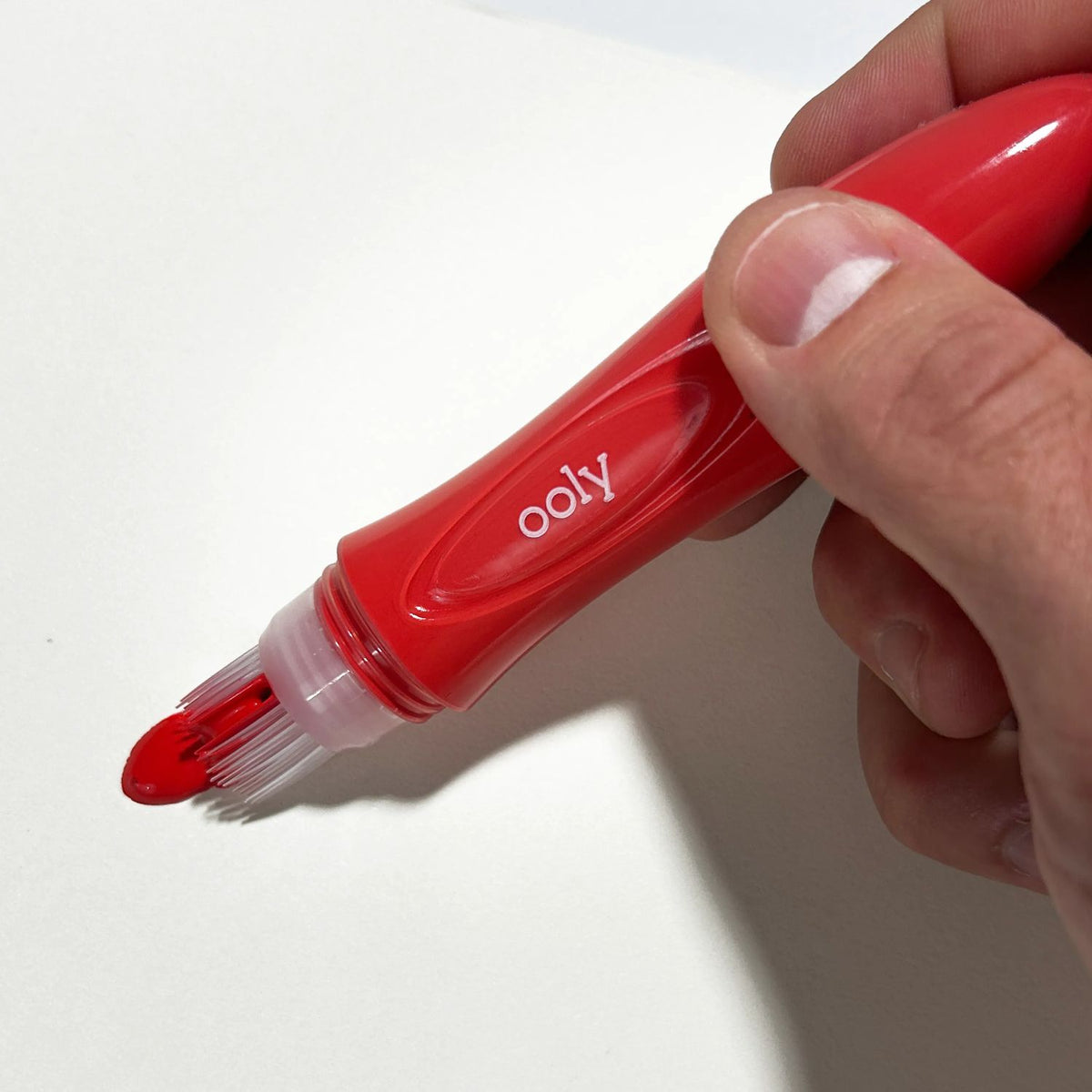 Red marker with &#39;ooly&#39; branding held by a hand on a white background