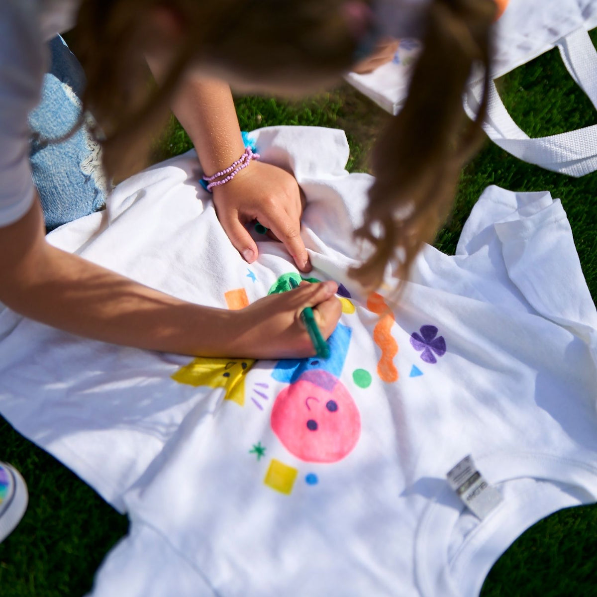 Two children drawing on a white blanket with colorful markers outdoors.