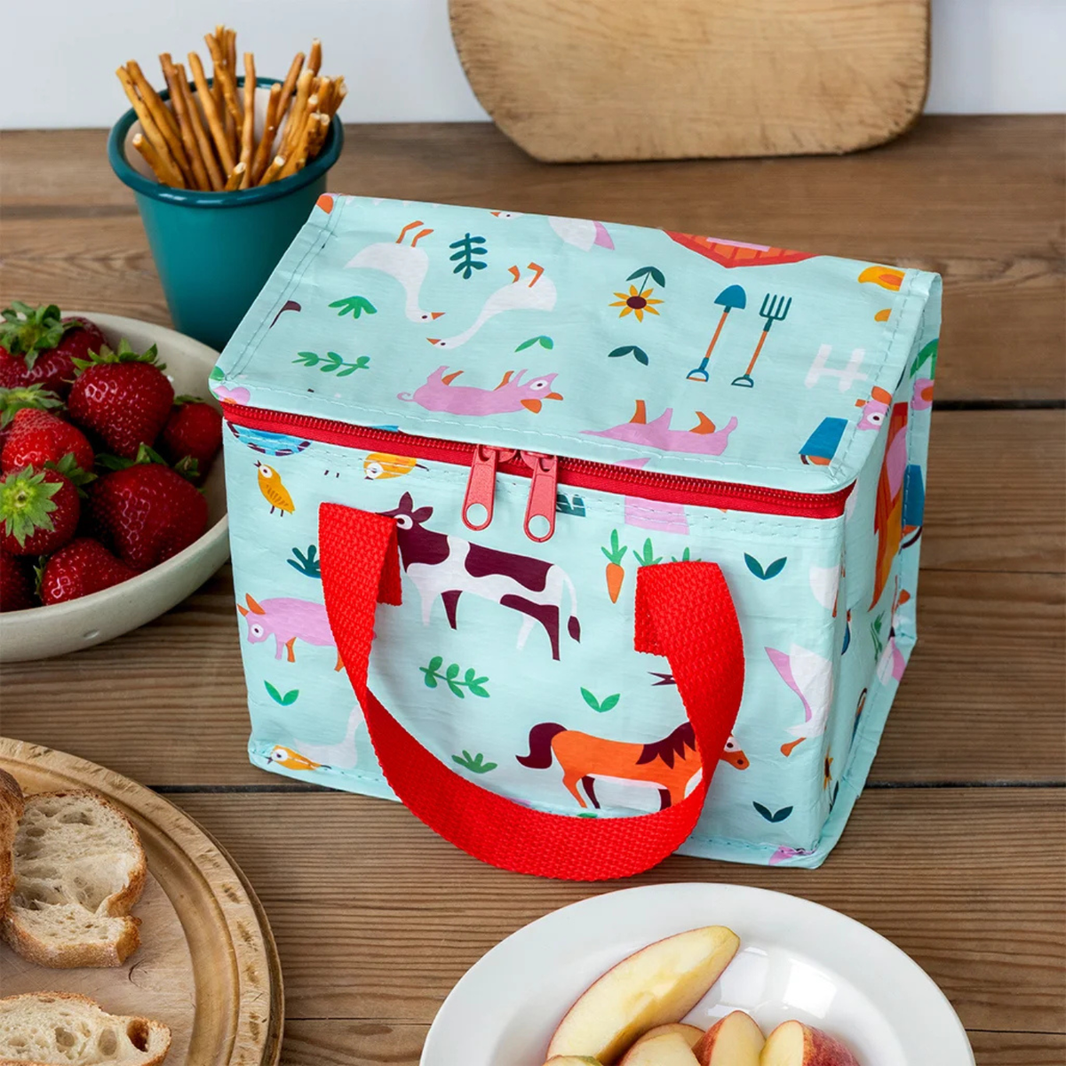 Colorful insulated lunch bag with farm animal pattern on a wooden table with snacks.