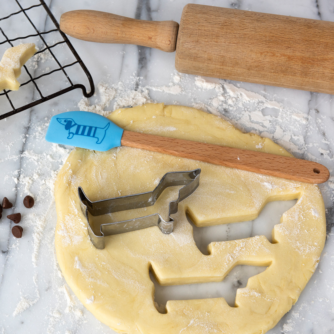 Baking tools including a rolling pin, spatula, and sausage dog cookie cutter on a piece of dough.