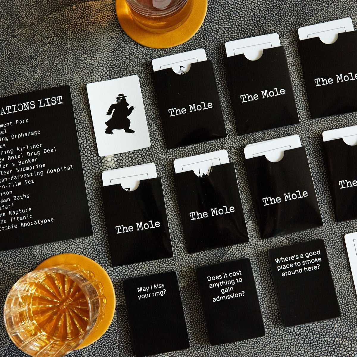 Set of cards with 'The Mole' and other text on a textured surface with drinks.