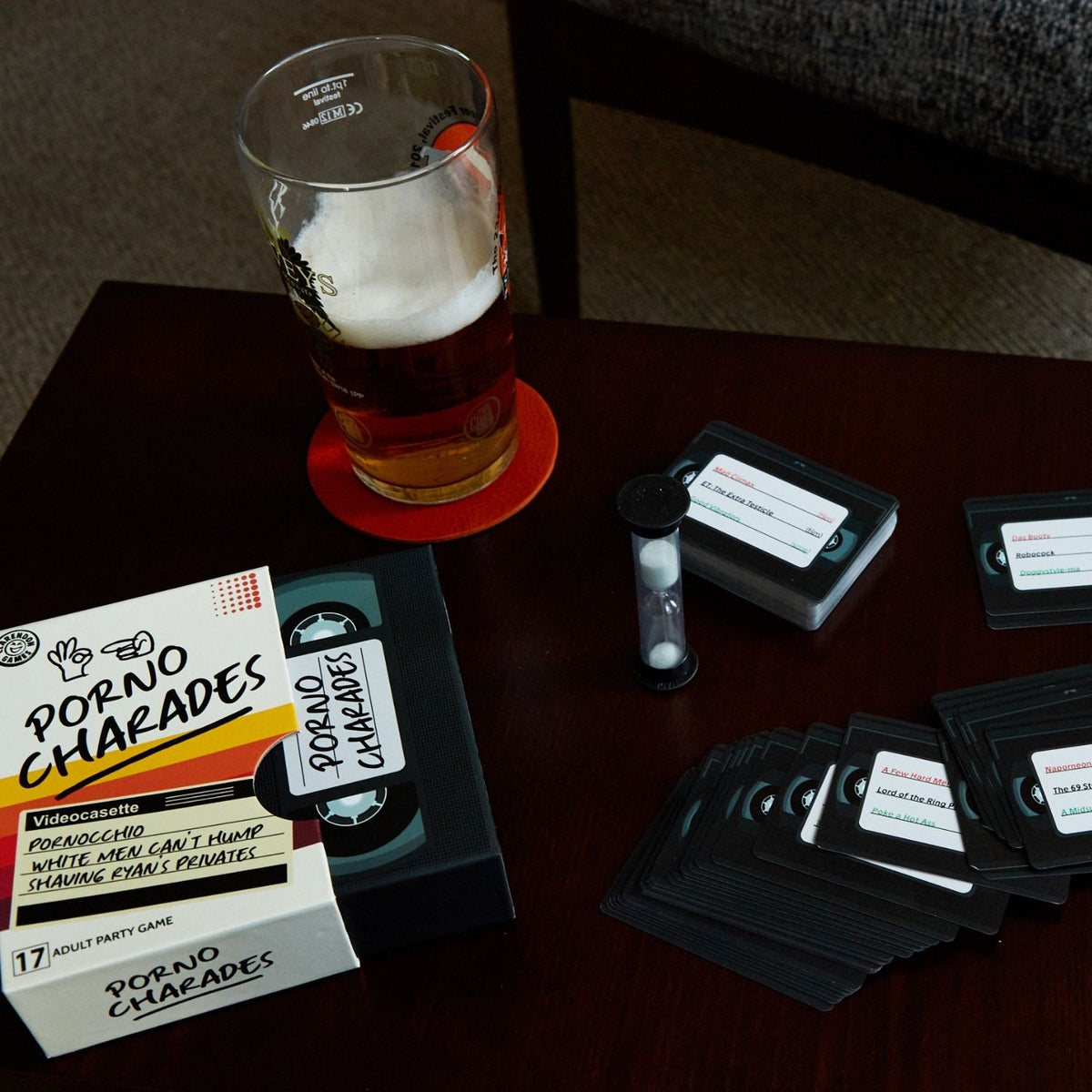 Porno Charades game components on a table with a glass of beer.