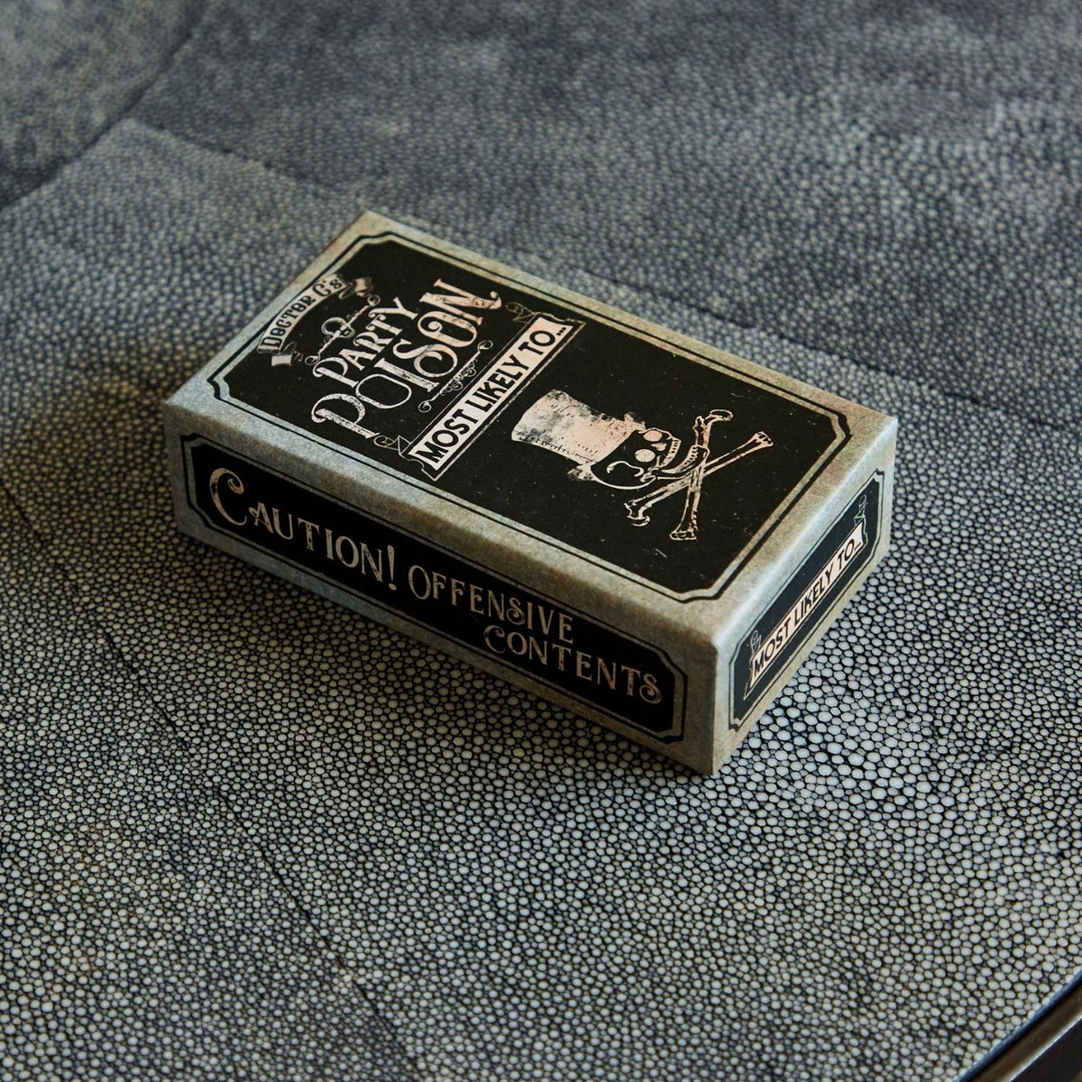 Playing card box labeled 'Party Poison' on a textured surface