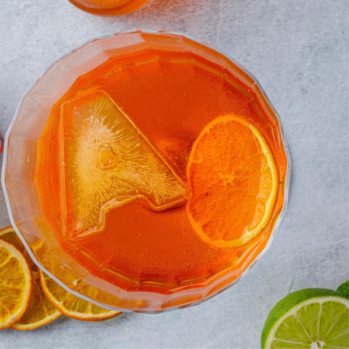 Orange jelly with a cube of ice and orange slices on a gray surface