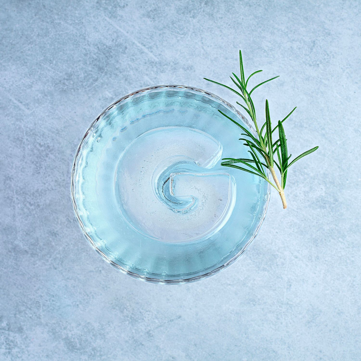 Blue cocktail in a glass with a sprig of rosemary on a light blue background