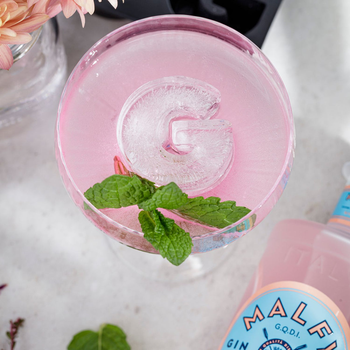 Pink cocktail with ice and mint leaves, featuring a bottle of Malibu rum.