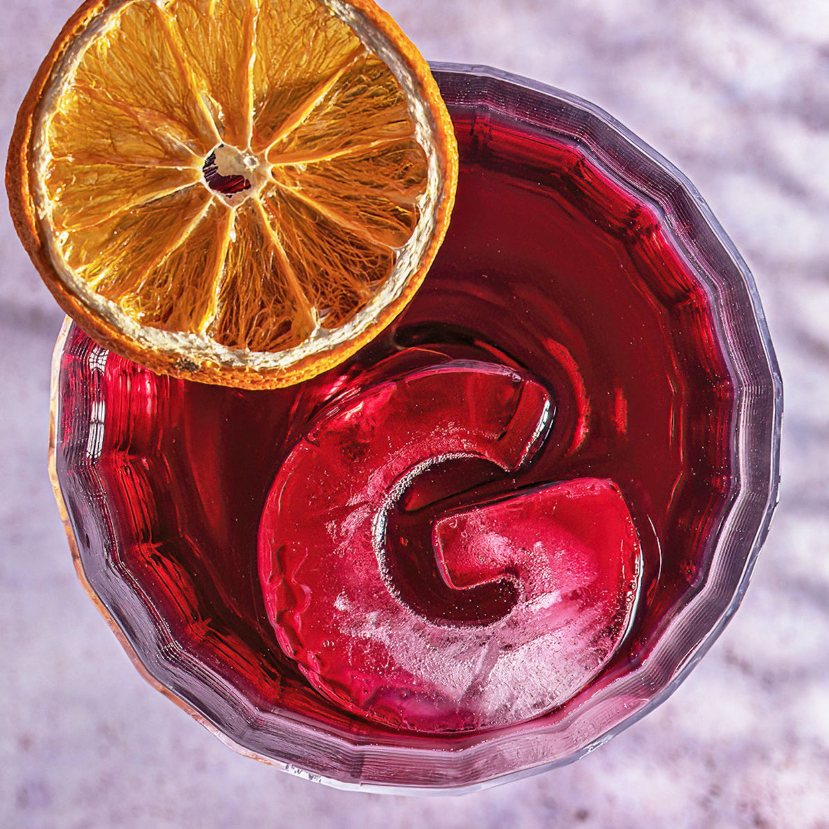 Red cocktail with an orange slice in a glass on a textured surface