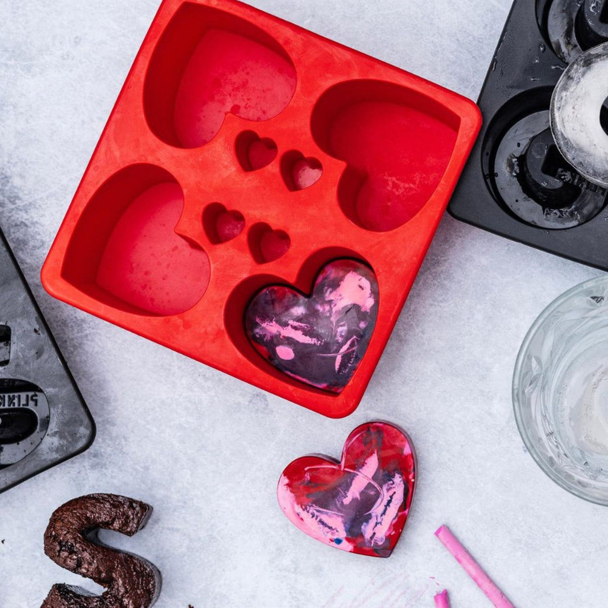 Red heart-shaped silicone mold with pink and red heart-shaped objects on a gray surface.