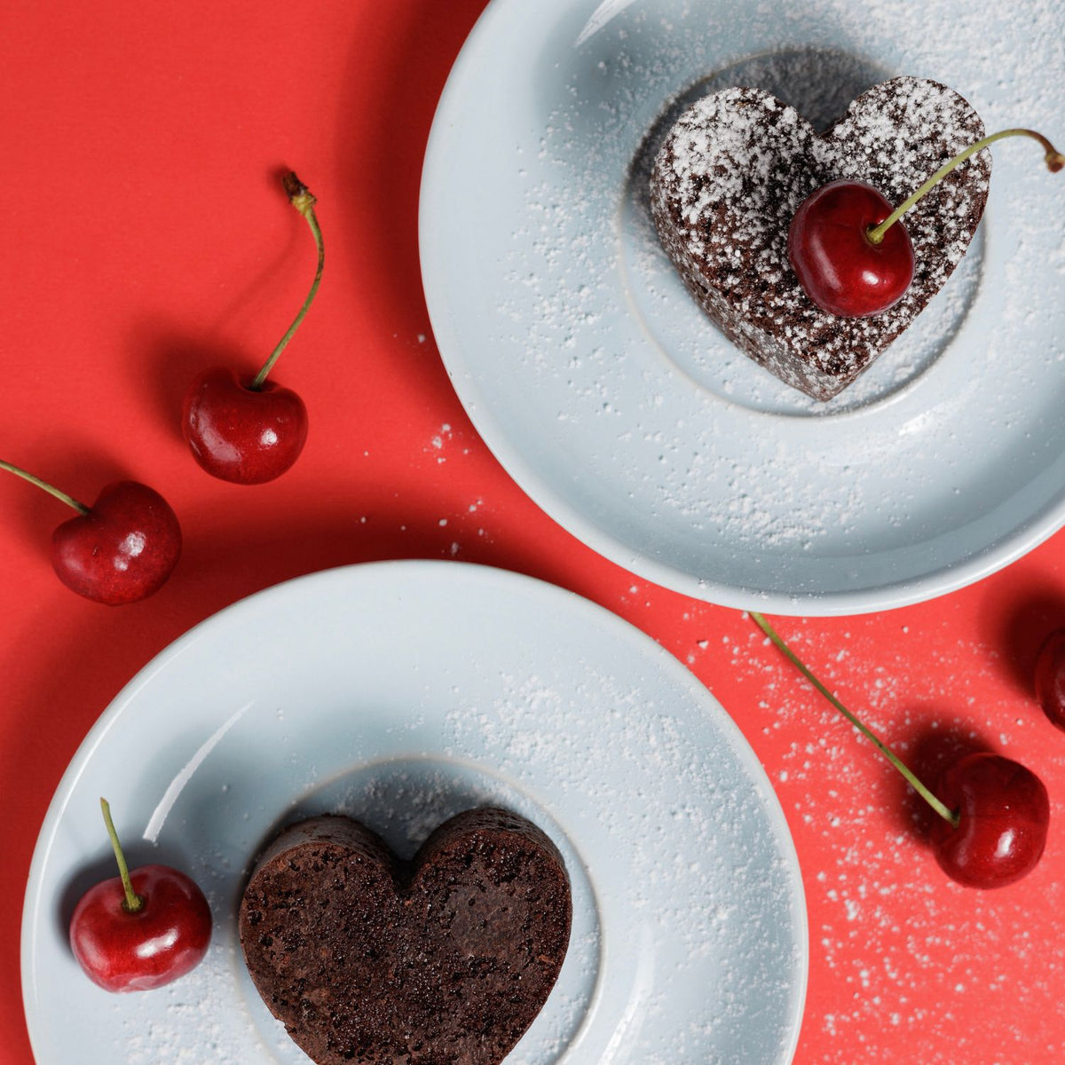 Heart-shaped chocolate cakes with cherries on a red background