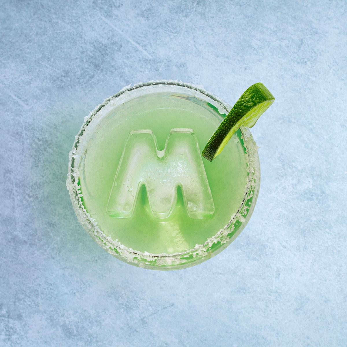 Green cocktail with a lime wedge on a textured blue surface