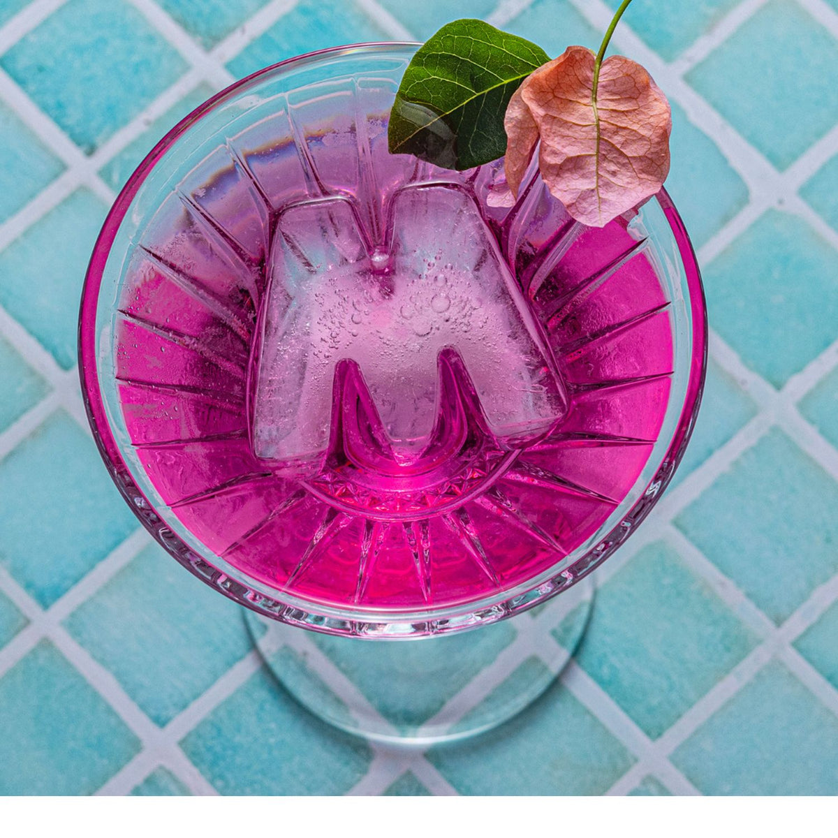 Pink cocktail in a glass with ice and leaves on a blue checkered background
