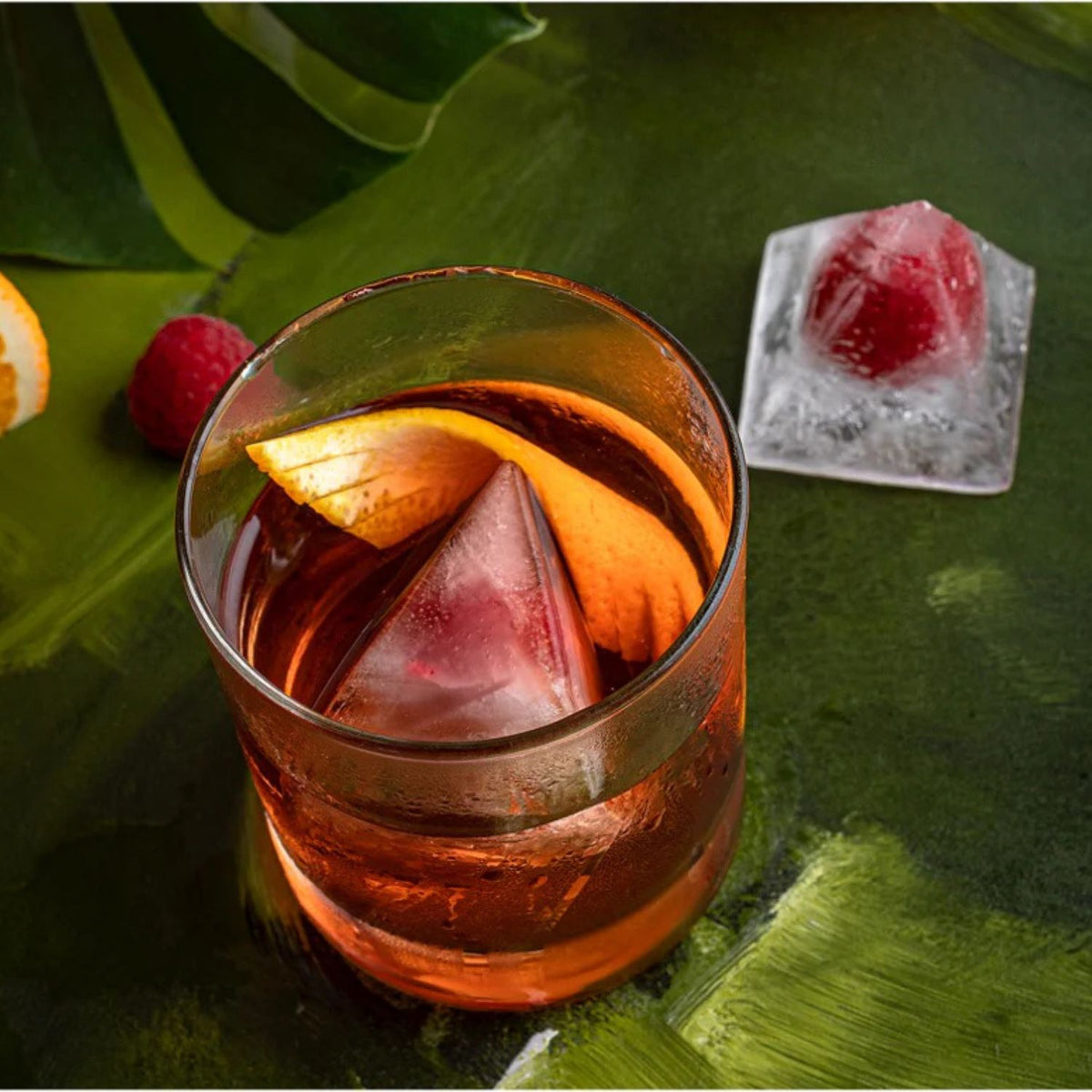 Cocktail with ice cubes and fruit in a glass on a green leafy background