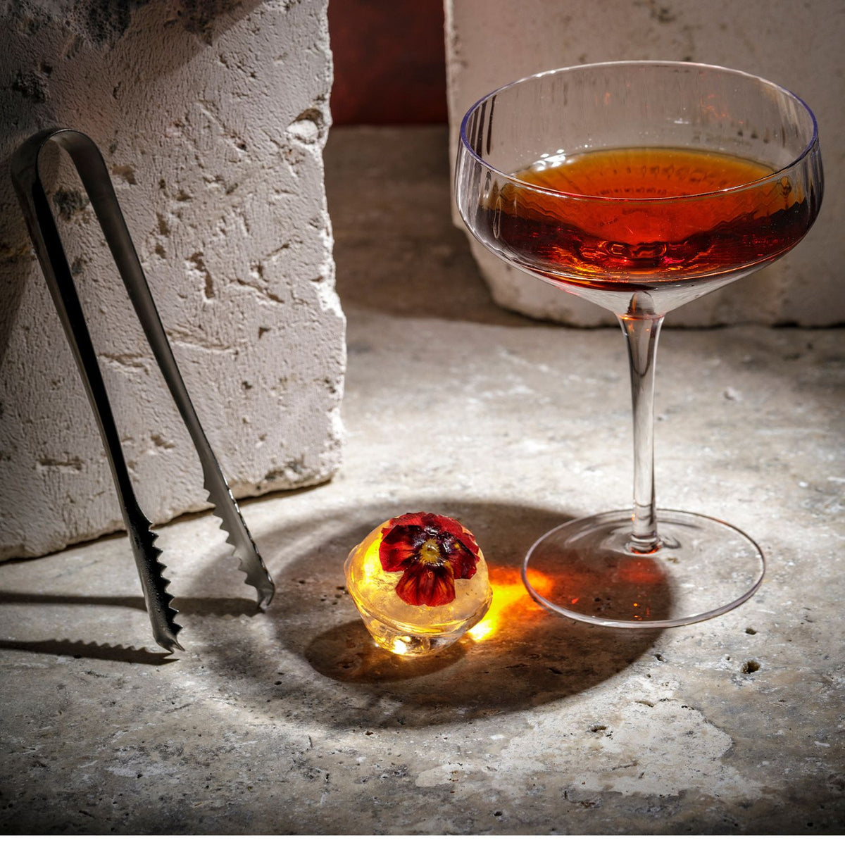 Cocktail glass with a red flower garnish on a textured surface