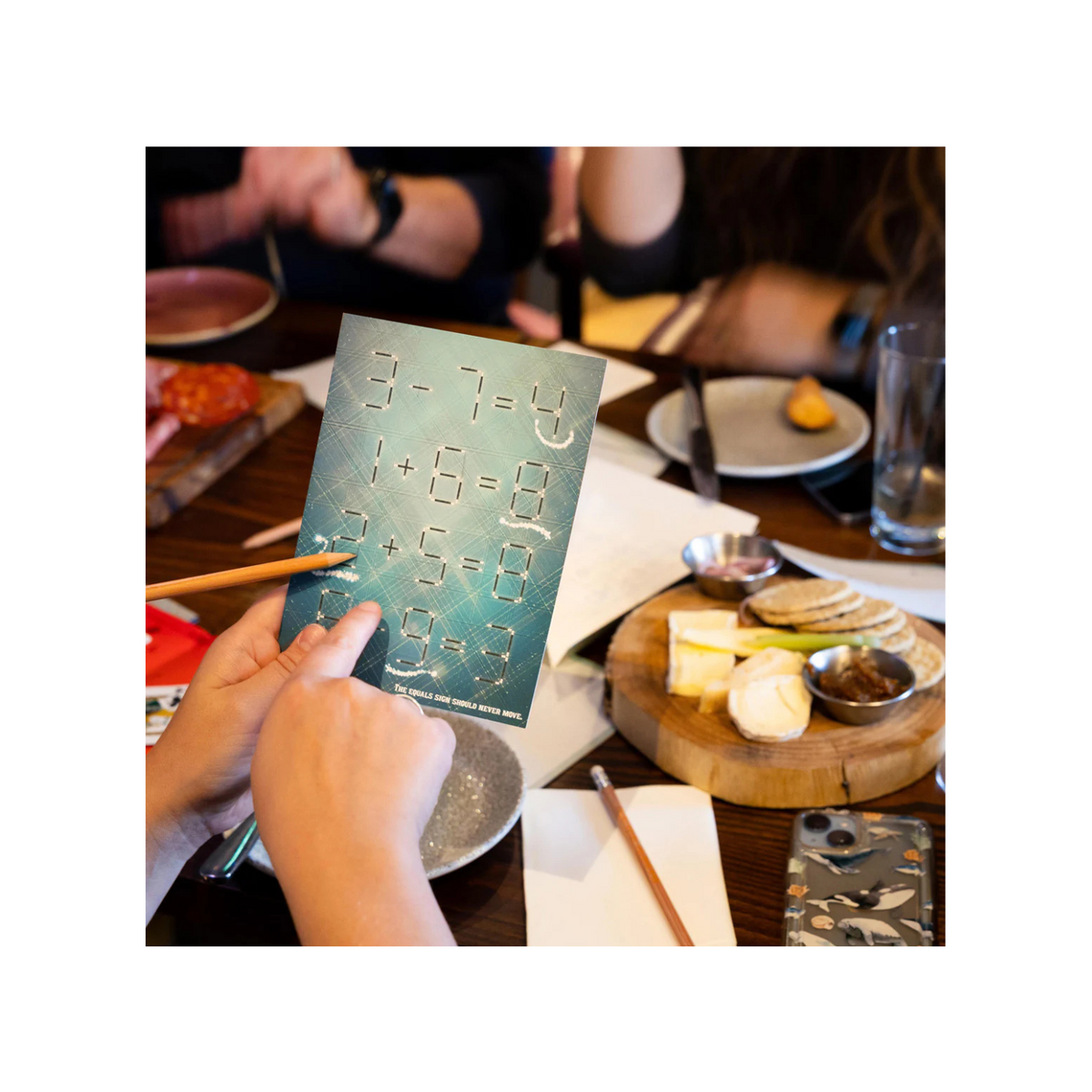 Person holding a card with mathematical equations at a dining table with food and cutlery.