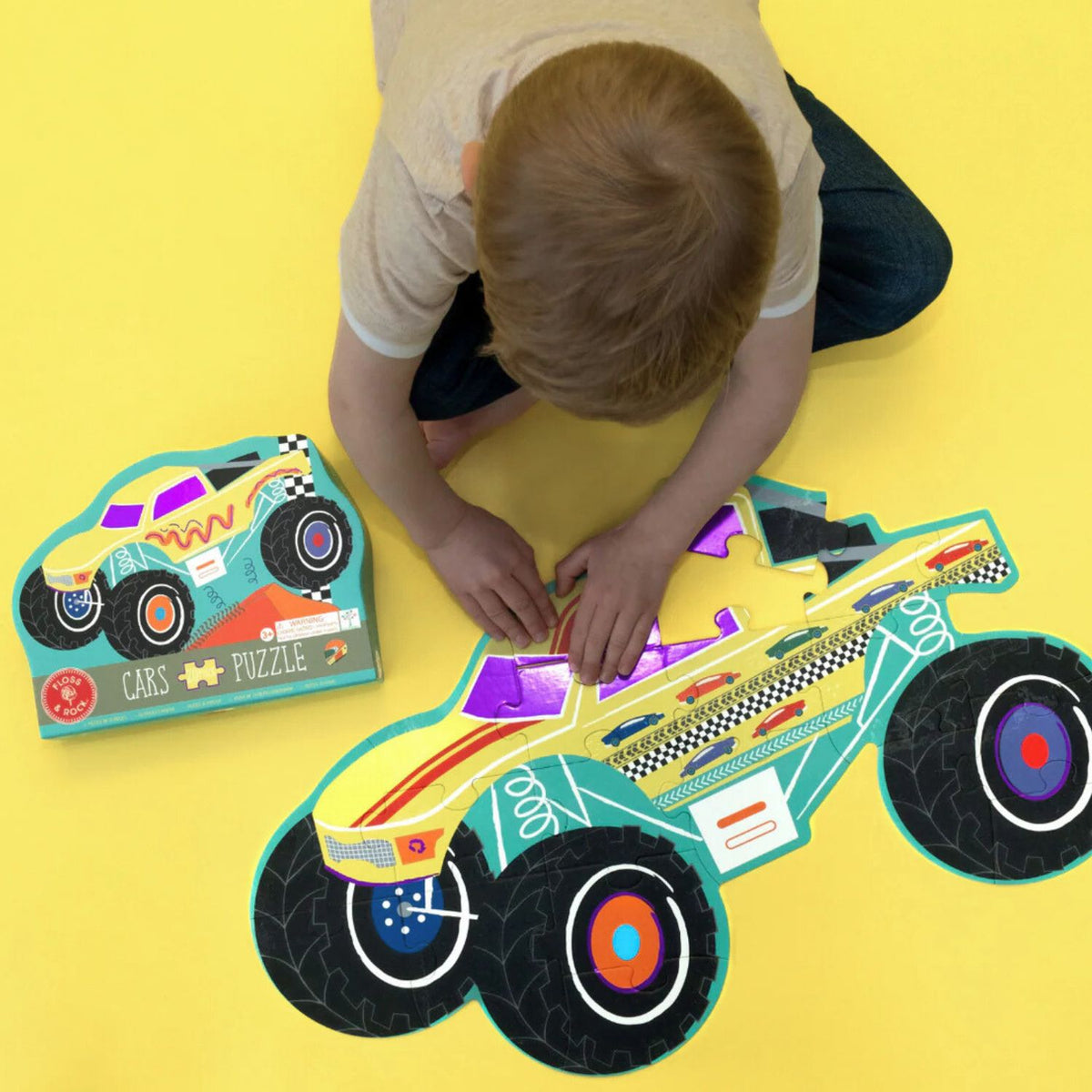 A close-up of a child’s hand holding a thick, chunky monster truck puzzle piece, showcasing the durability and the bright, soy-ink-printed colors.