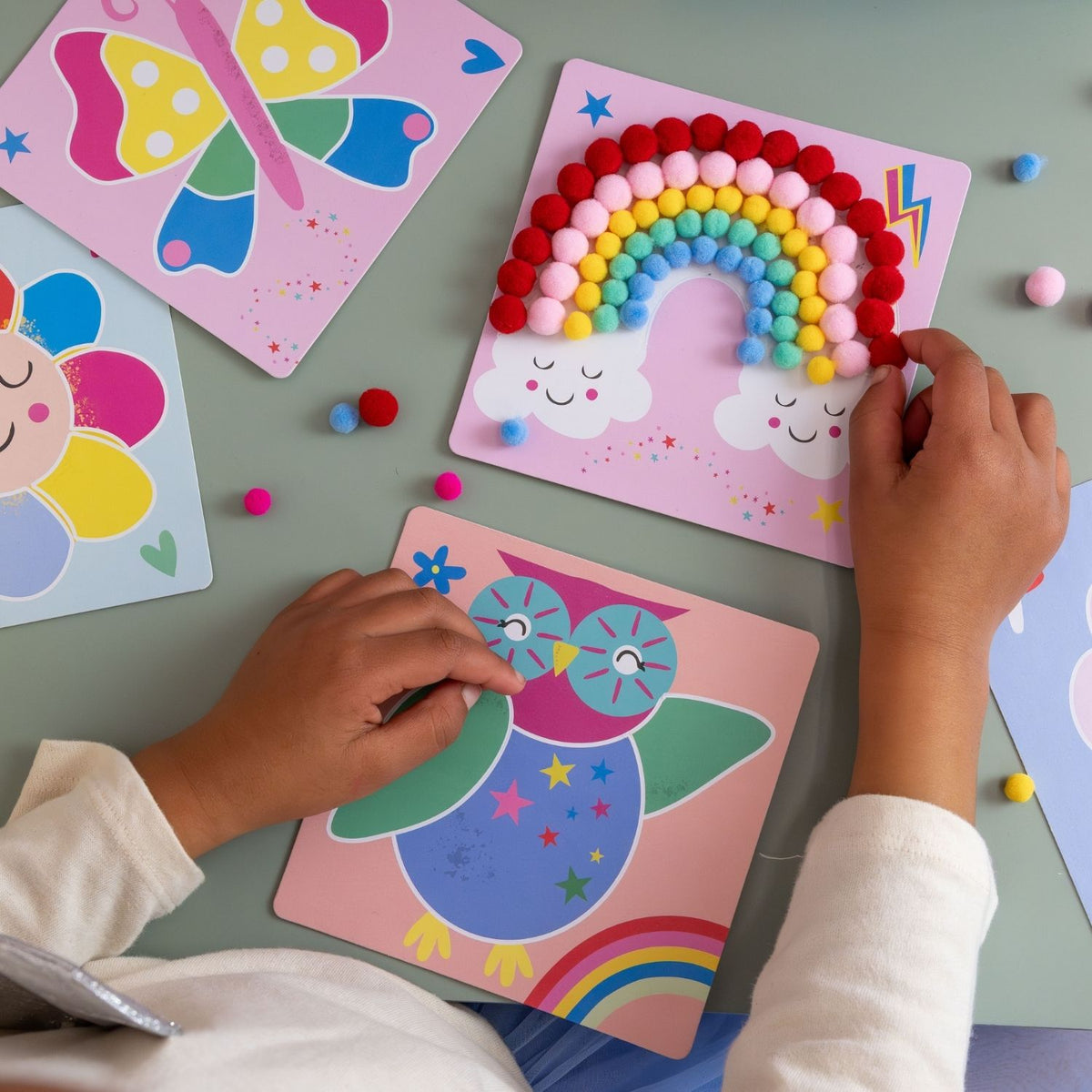 A finished pom pom art piece of a colourful rainbow and sun sitting on a child's bedside table, showcasing the tactile texture and vibrant colours.