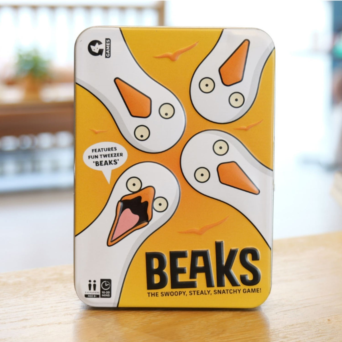 Game tin for 'Beaks' with cartoon seagull faces on a blurred background