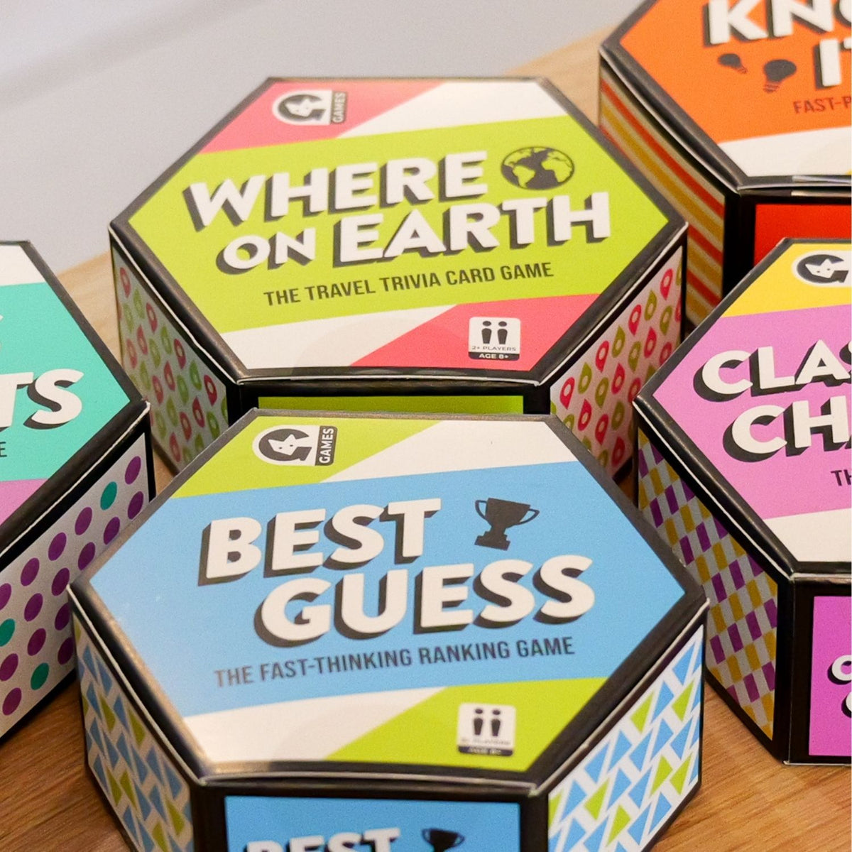 Hexagonal boxes of board games including 'Where on Earth' and 'Best Guess' on a wooden surface.