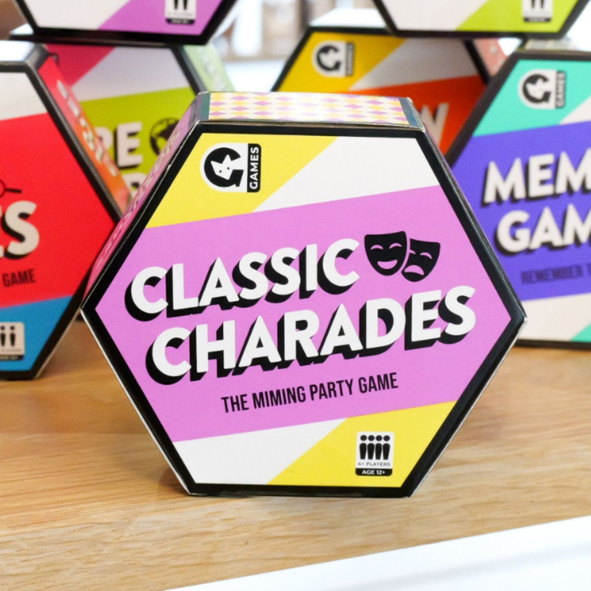 Hexagonal 'Classic Charades' game box on a wooden surface with other game boxes in the background.