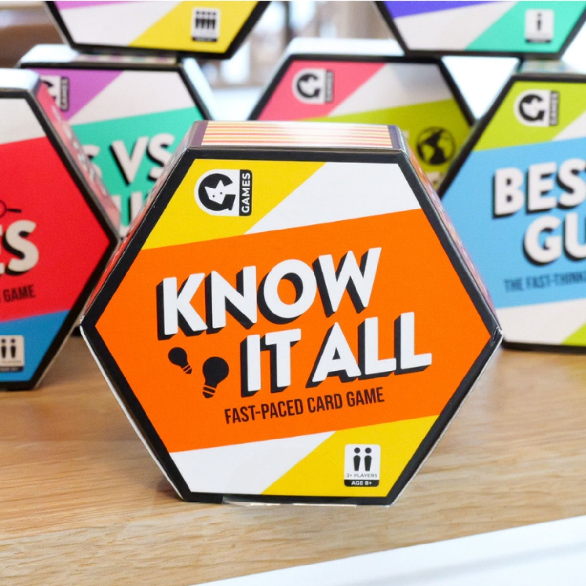 Hexagonal 'Know It All' card game box on a wooden surface with other game boxes in the background.