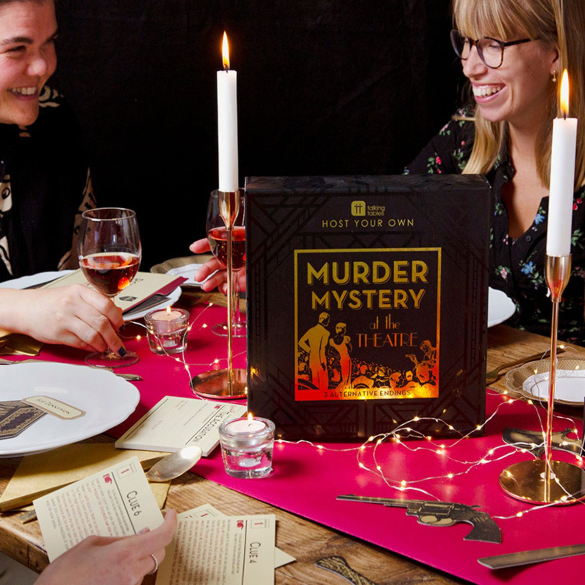 Two people at a dinner table with a murder mystery game box, candles, and wine glasses.