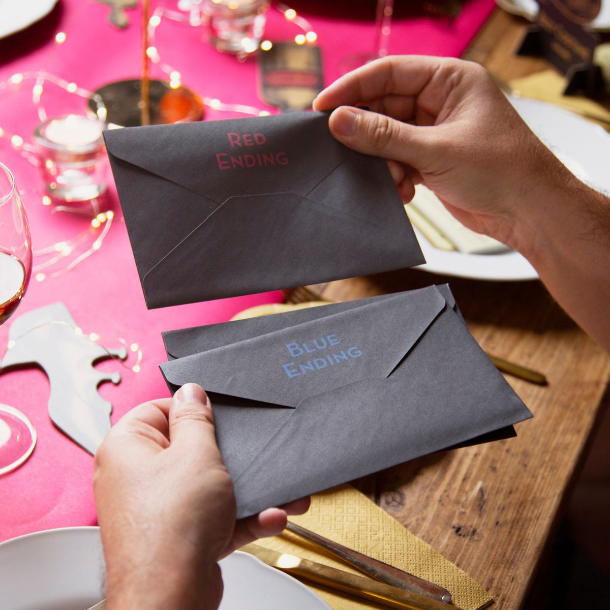 Two hands holding gray envelopes labeled &#39;Red Ending&#39; and &#39;Blue Ending&#39; on a festive table.