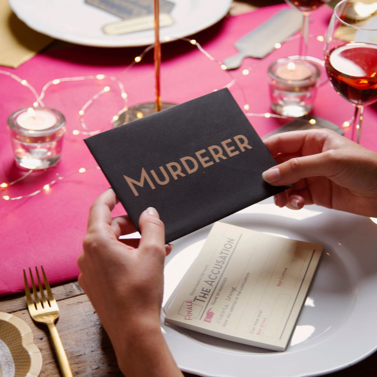Person holding a book titled &#39;Murderer&#39; on a table setting with candles and glasses.