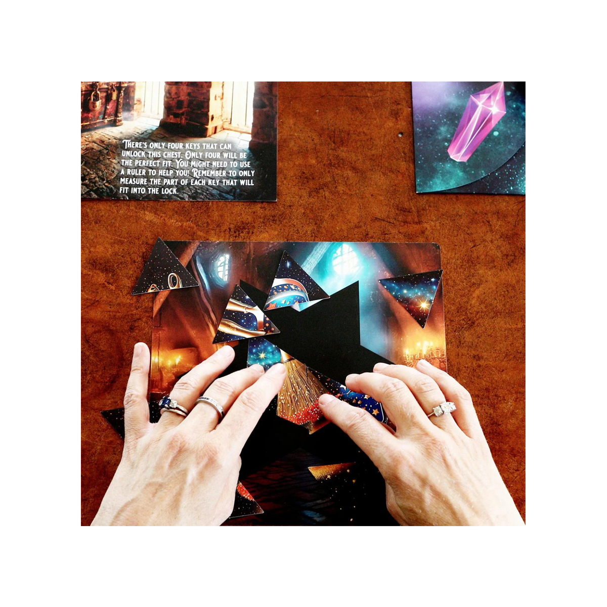 Two hands holding a deck of cards over a wooden surface with tarot cards and a crystal on a white background.