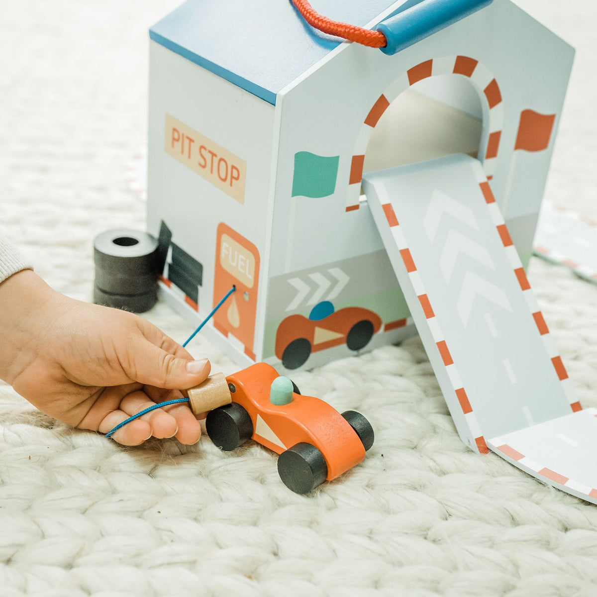 A close-up shot of a toddler’s hand zooming a red wooden race car across to the pit stop, capturing active fine motor play.