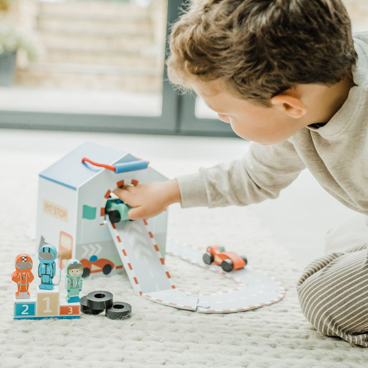 Child playing with the toy racing car play set on a wooden track set up on the floor.