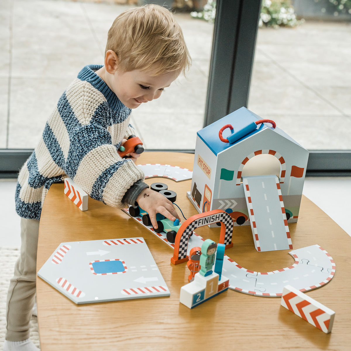 Child playing with a wooden toy race track play set on a table.