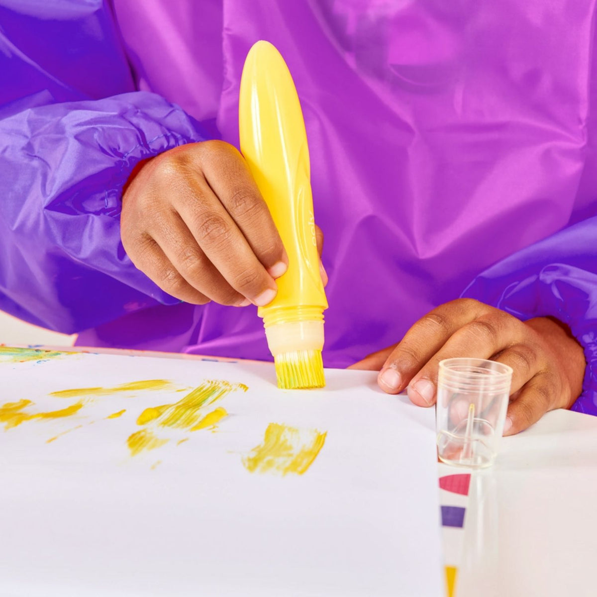 Child's hand holding a yellow marker with a purple raincoat in the background