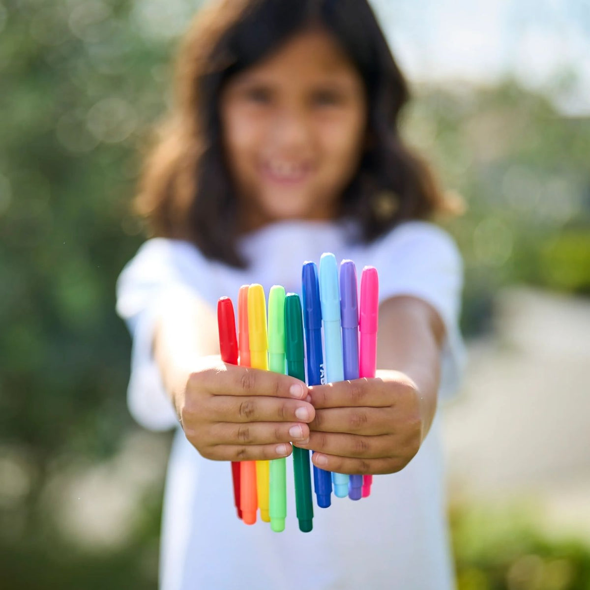 Child holding colorful fabric markers with a blurred natural background