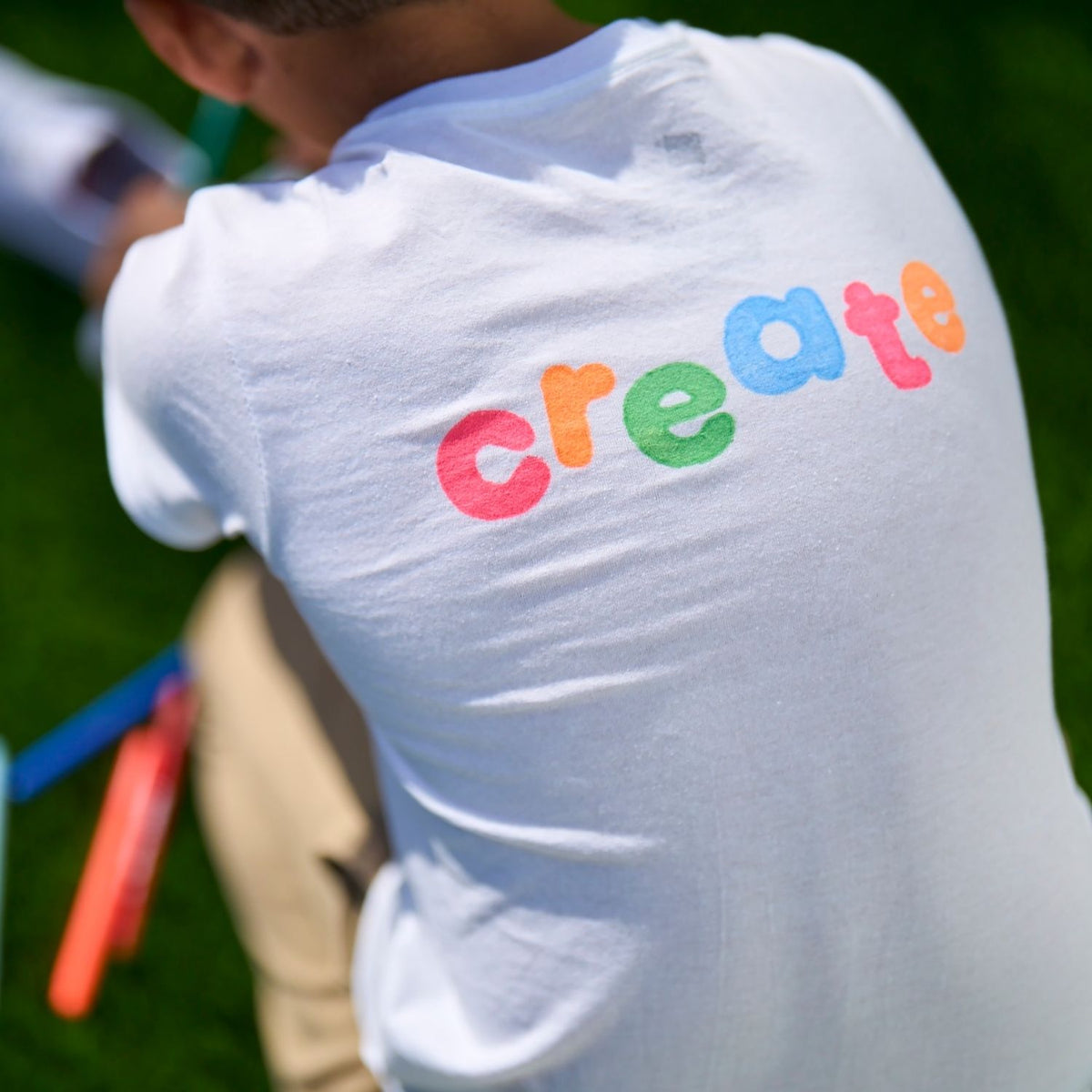 White t-shirt with colorful 'create' text on a child's back, outdoors.