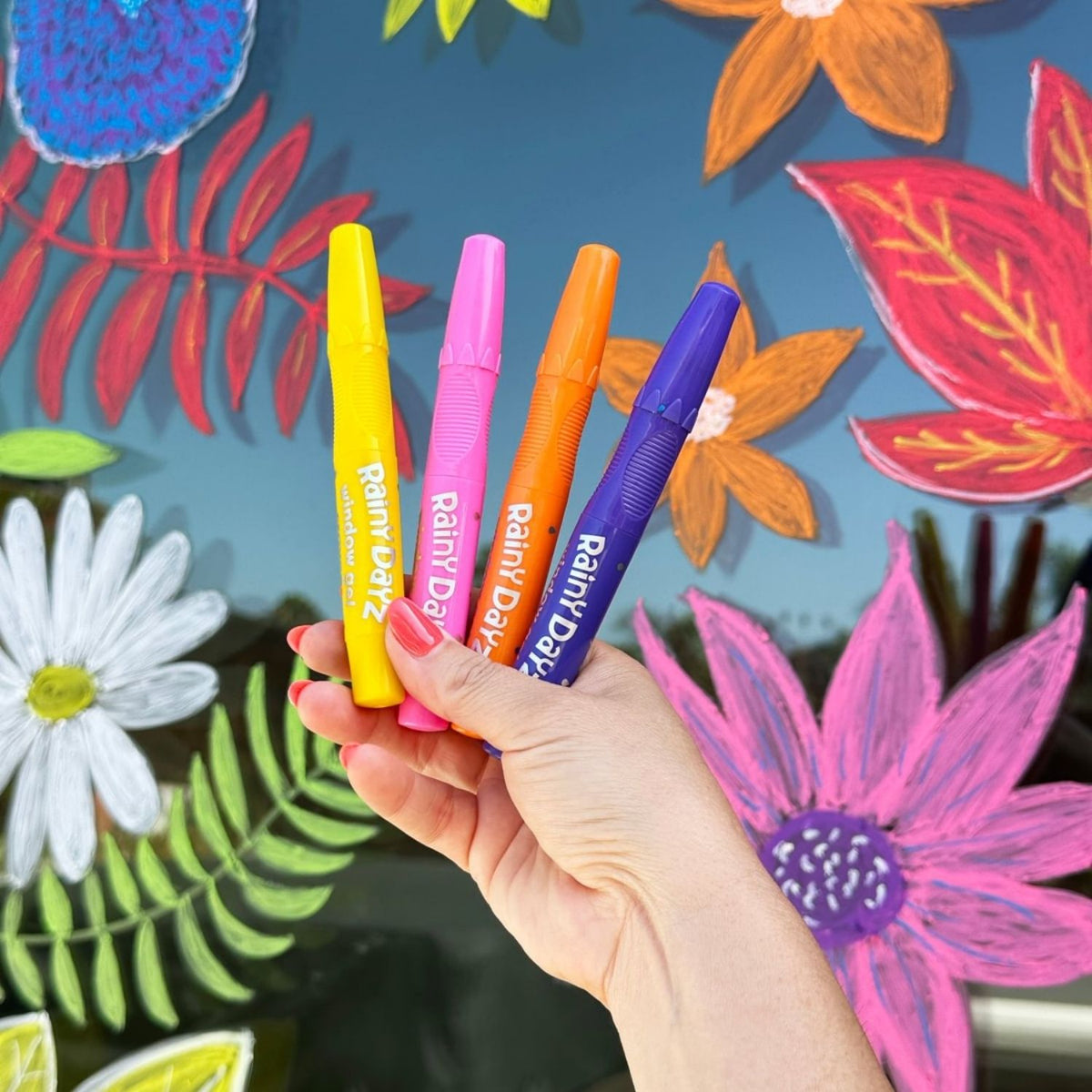 Hand holding four colorful gel crayons with a floral design on a shop window
