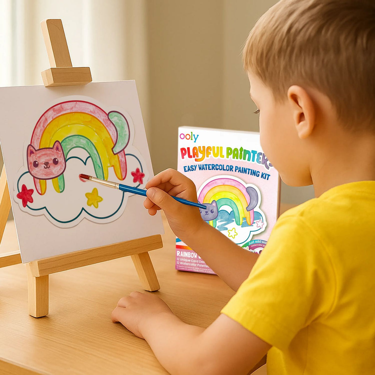 Child painting a rainbow with a pink cat on a canvas, using an Ooly Playful Painters kit.