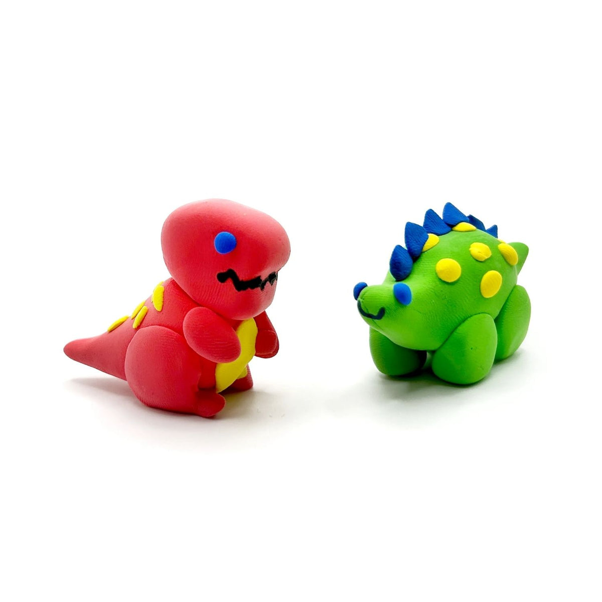 The completed clay T-Rex and Stegosaurus standing together, showcasing the smooth, matte finish of the air-hardened clay.