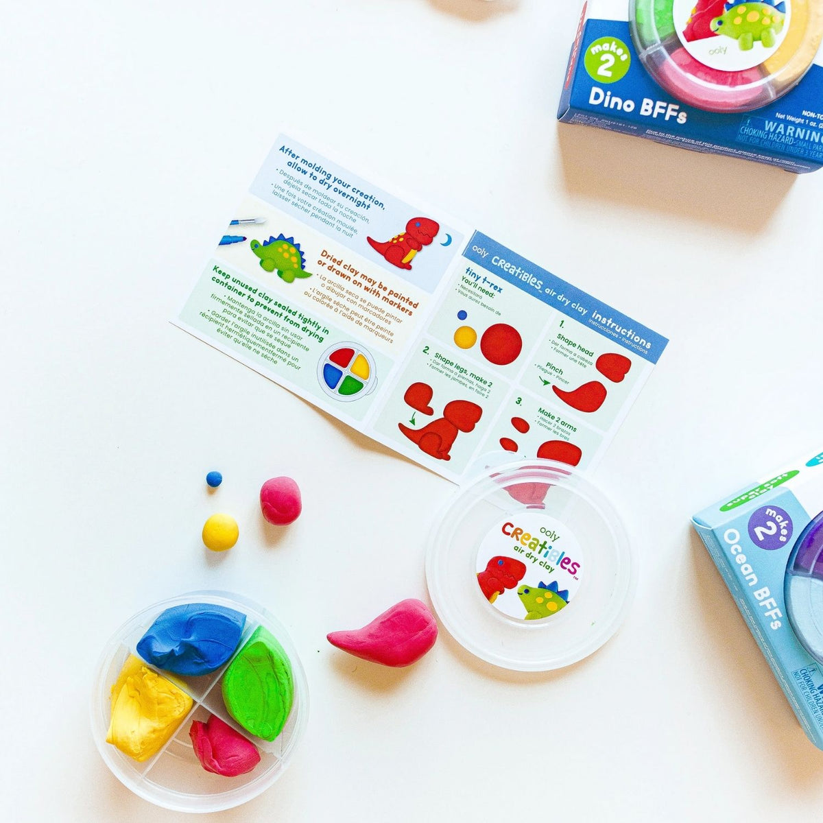 The Dino BFFs Air Dry Clay kit in its compact, reusable storage tub, featuring bright labels and illustrations of the T-Rex and Stegosaurus characters.