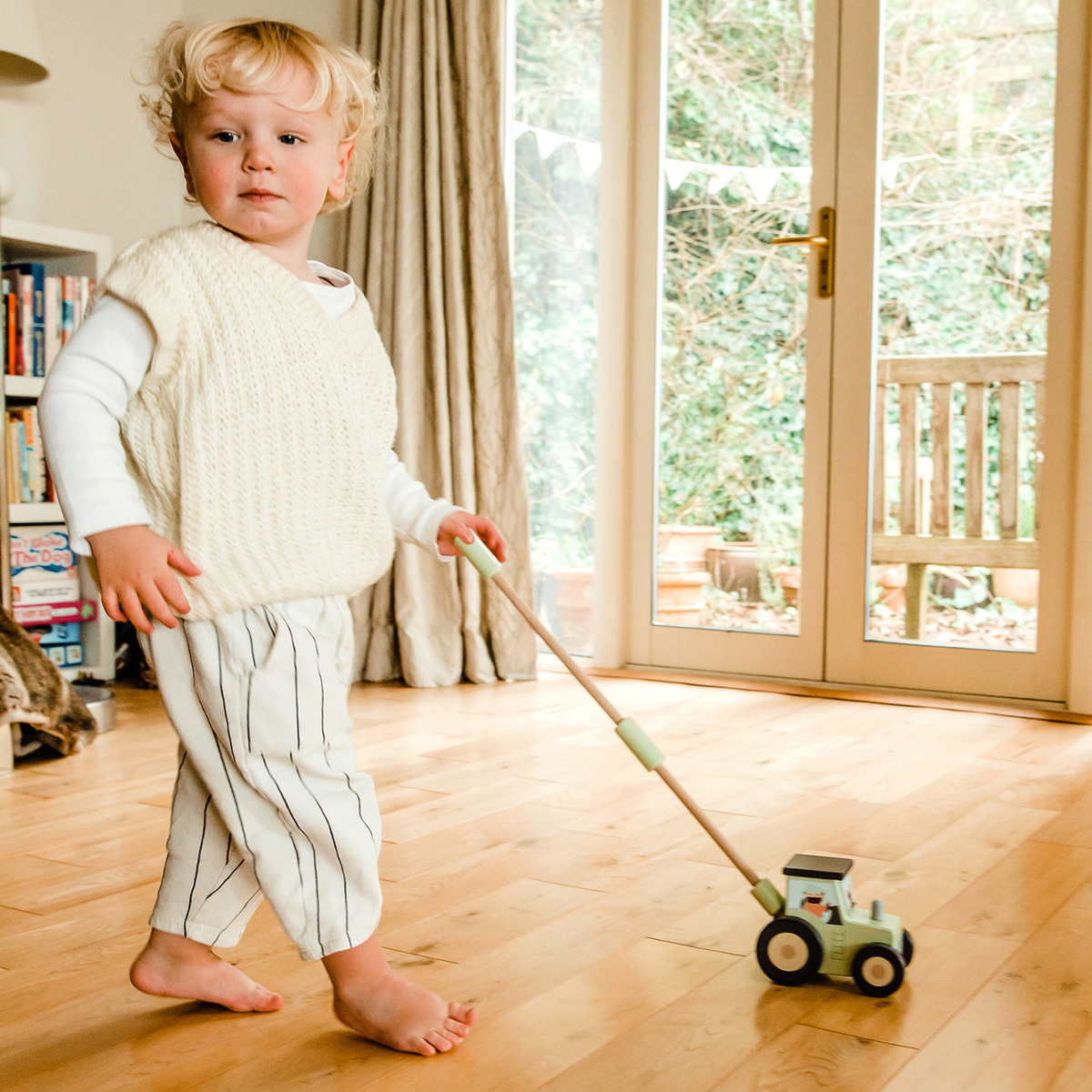 A young child’s hands gripping the smooth wooden ball topper of the push along, ready to push the tractor forward across the floor.