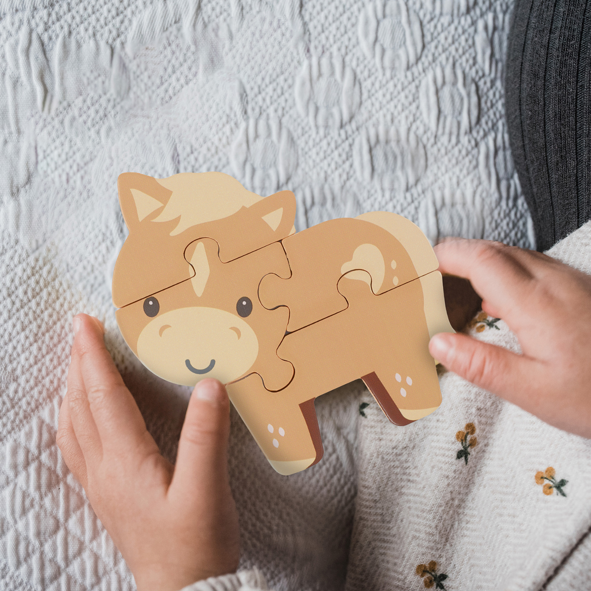 A close-up shot of a toddler’s small hands carefully fitting a chunky wooden jigsaw piece into place to complete the pony puzzle
