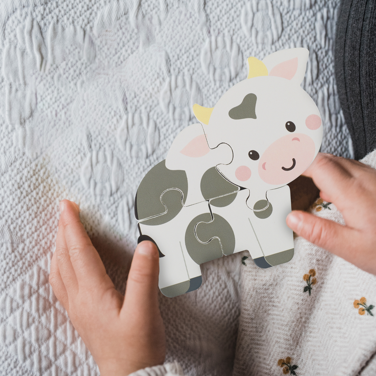 A close-up shot of a toddler’s small hands carefully connecting two chunky wooden pieces to complete the cow puzzle, illustrating fine motor control.