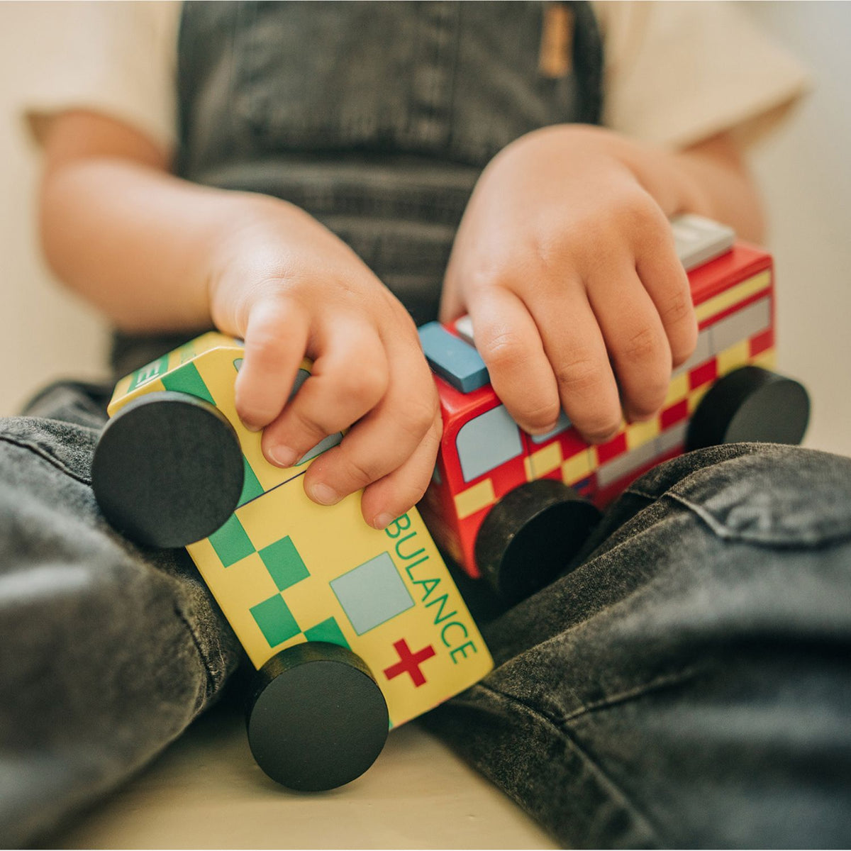 close-up shot of a toddler’s hand grasping the curved wooden roof of the fire engine and ambulance toys, demonstrating fine motor grip and movement.