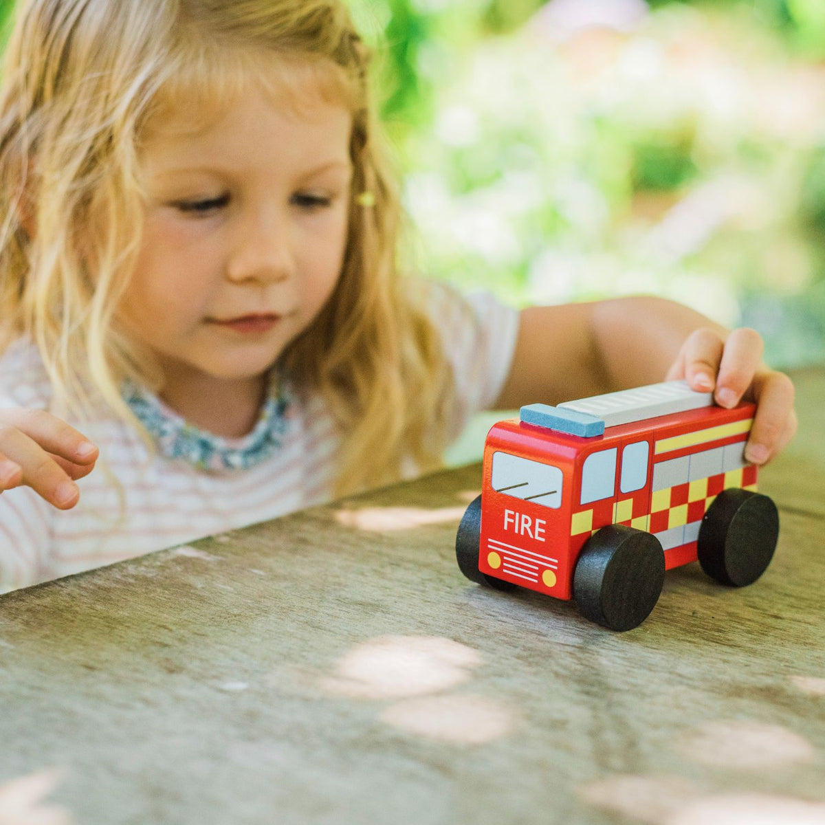 Child playing with a wooden fire truck toy outdoors