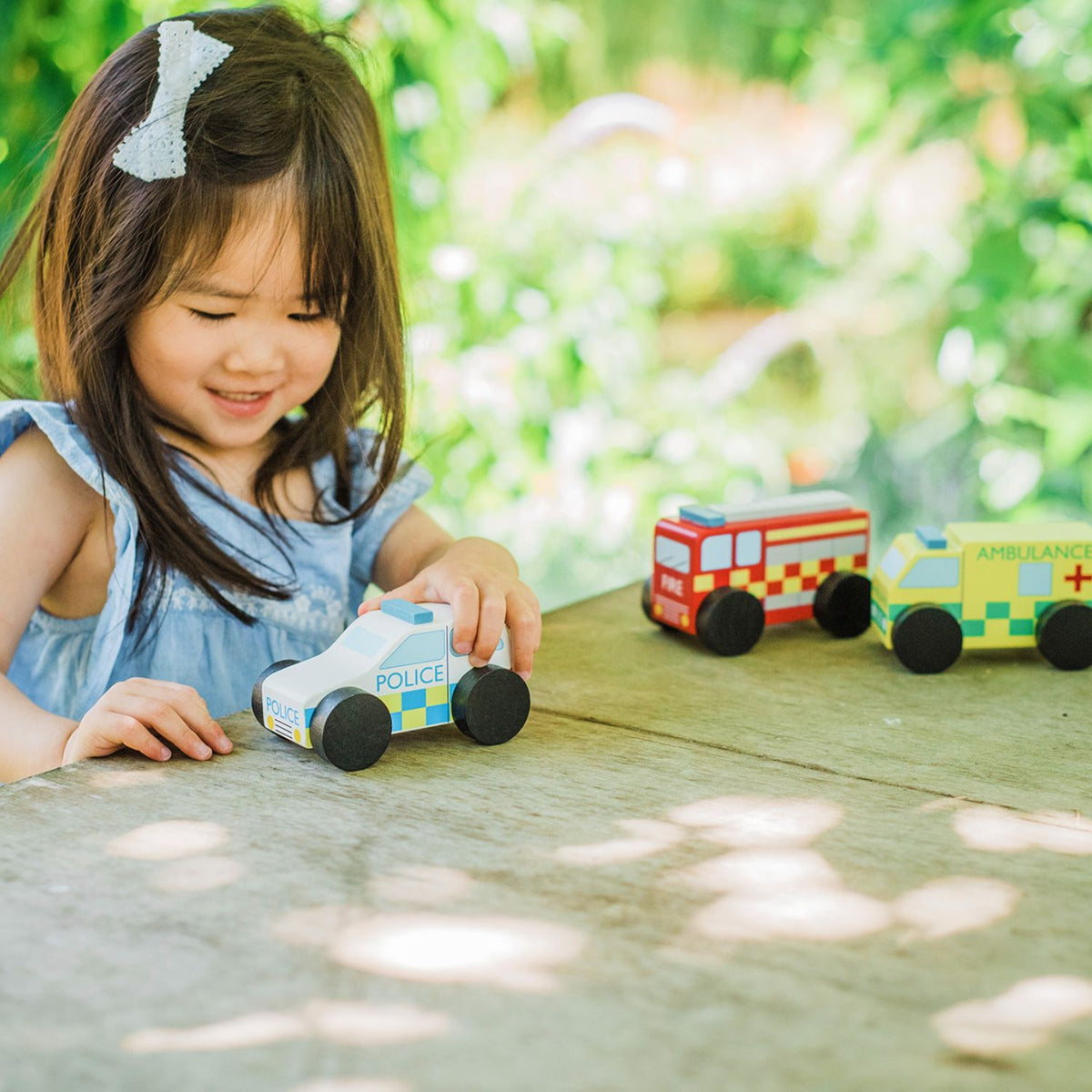 Child playing with toy police car on a wooden surface outdoors