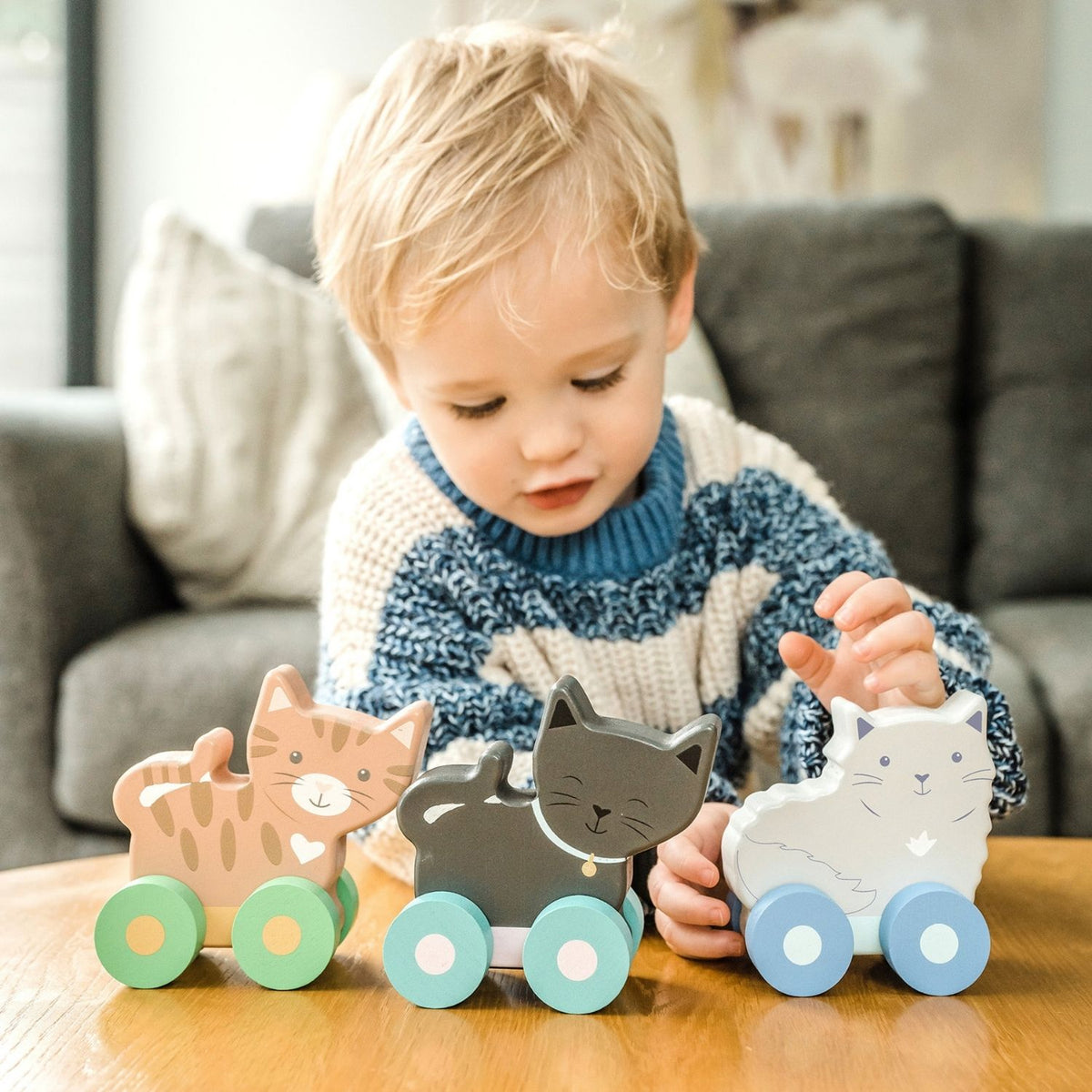 A toddler happily pushing a pastel wooden kitten forward, encouraging gross motor movement and physical coordination.