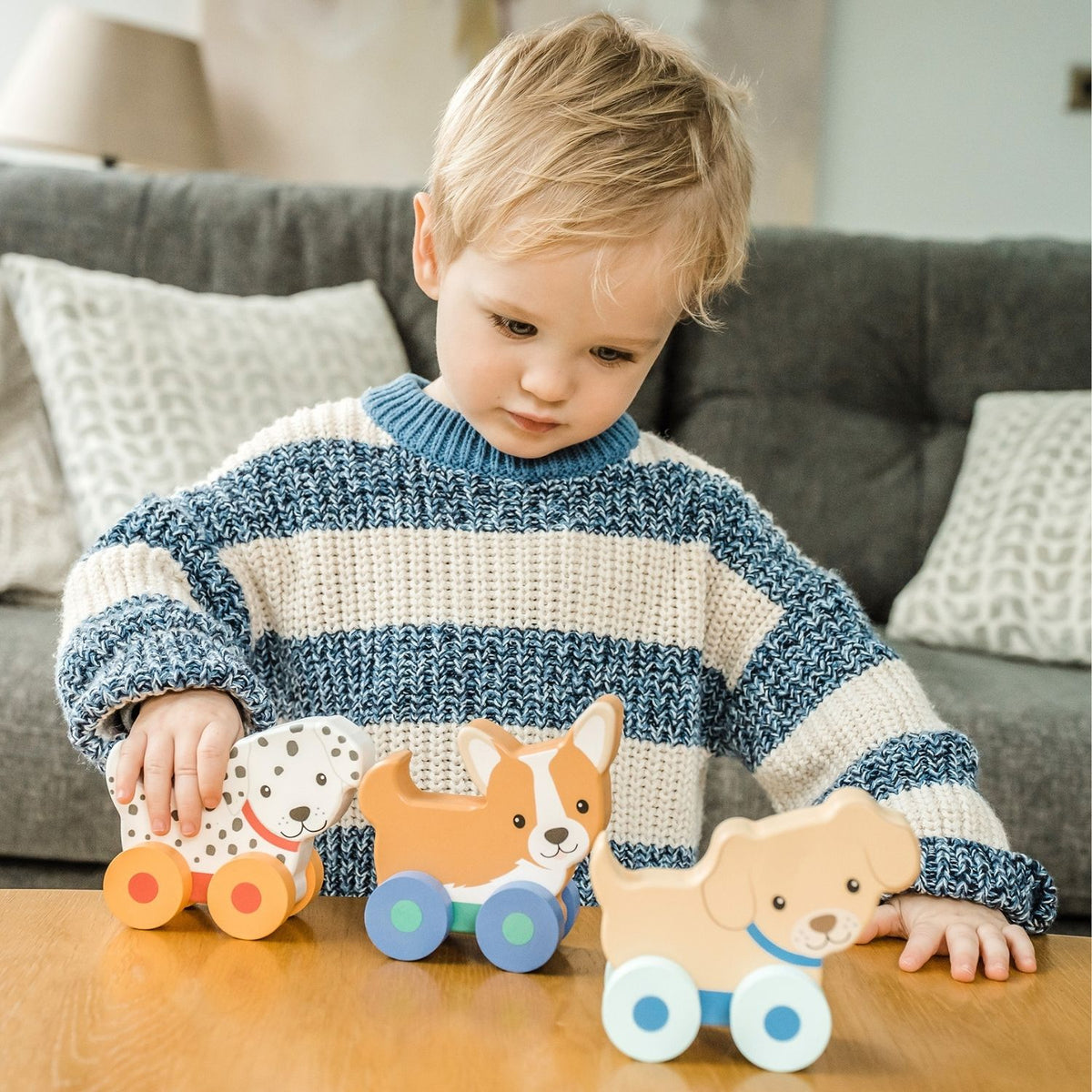 close-up shot of a toddler’s hand grasping the curved wooden back of a puppy toy and rolling it across a smooth wooden floor, demonstrating grip strength and fine motor play.