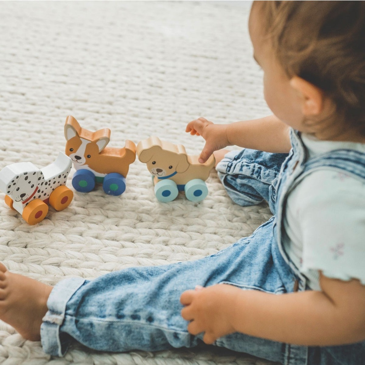 A close-up shot of a toddler’s hand reaching for a puppy toy and rolling it across the floor, demonstrating grip strength and fine motor play.