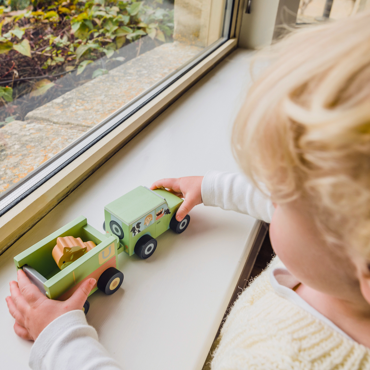 A young child pushing the hitched wooden 4x4 truck and horse float forward, demonstrating active gross motor play.