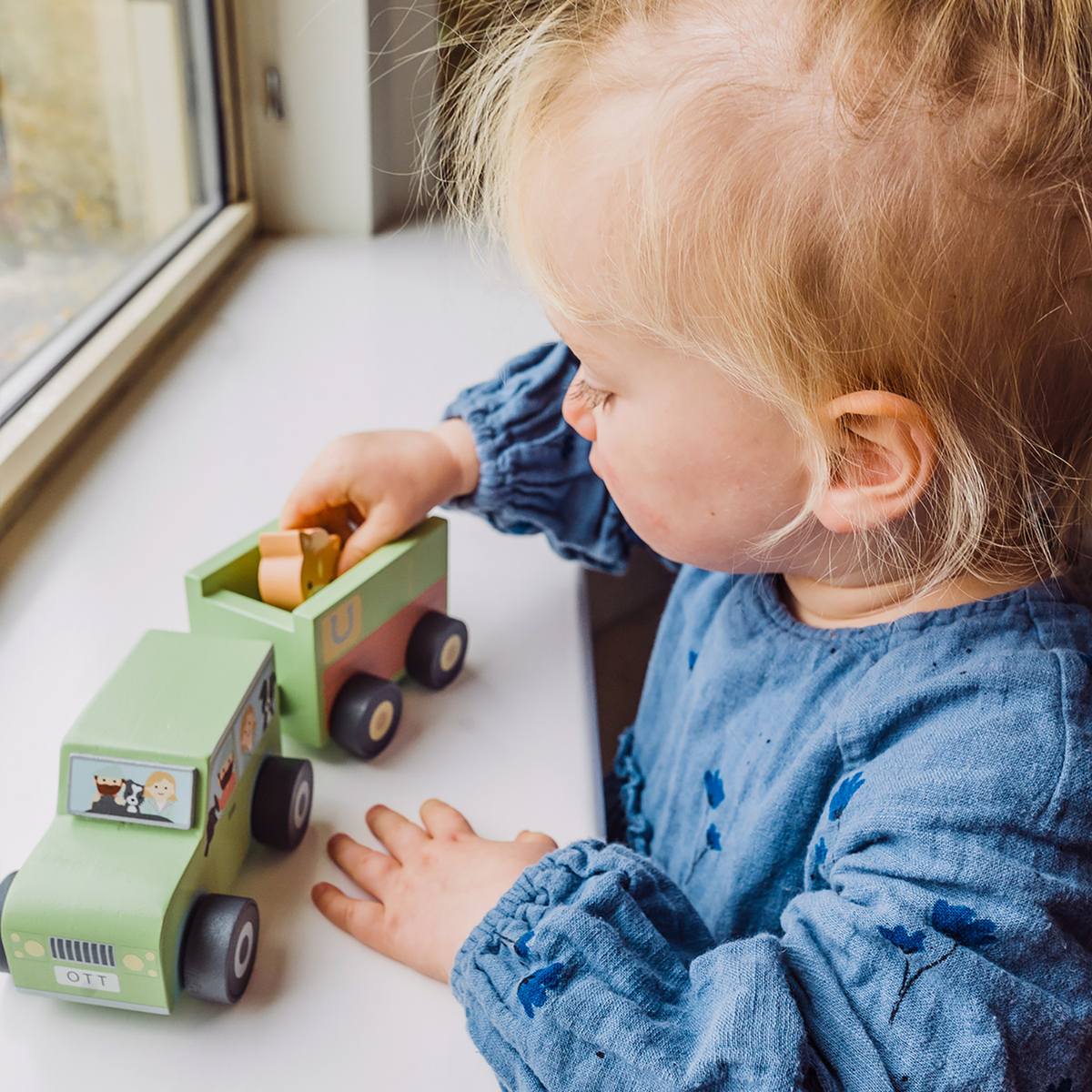 A close-up shot of a toddler’s hands carefully guiding the wooden horse into the horse float trailer, capturing fine motor focus.