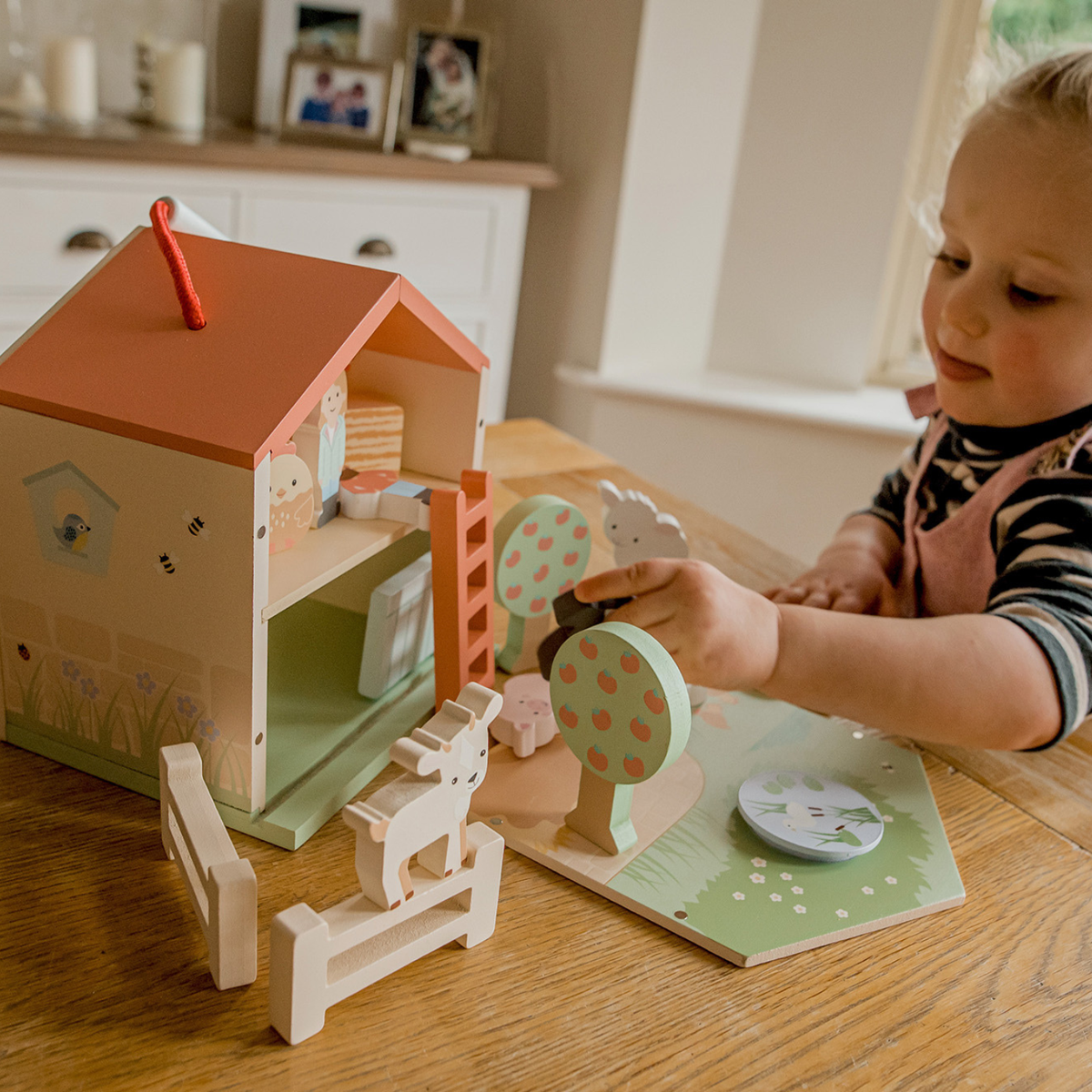 A close-up shot of a young child’s hands placing a painted wooden dog near the fold-out meadow and pond piece, capturing fine motor precision and small-world play.